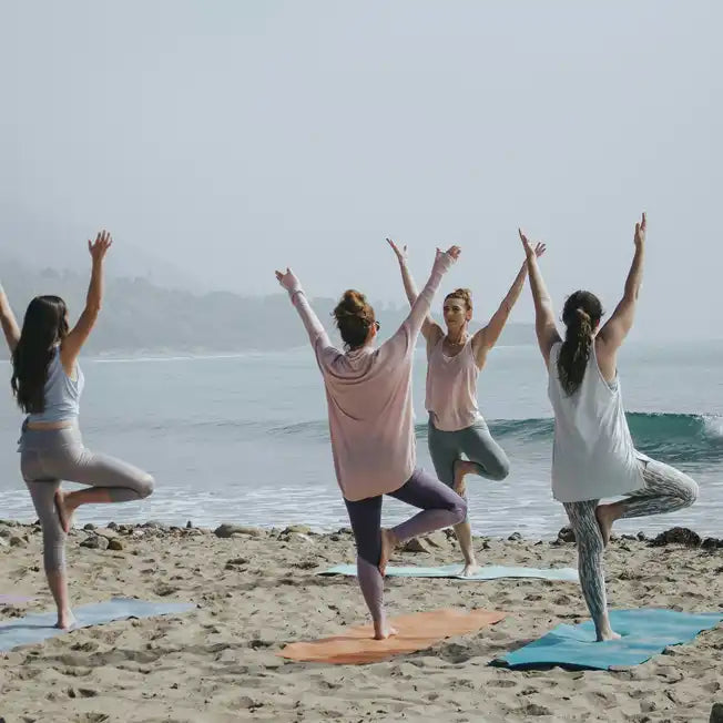 Four people practicing yoga poses together on colorful mats at the beach.