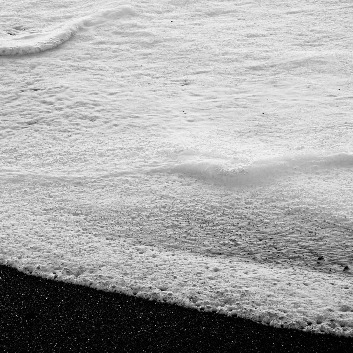 Foamy ocean wave washing over dark sand