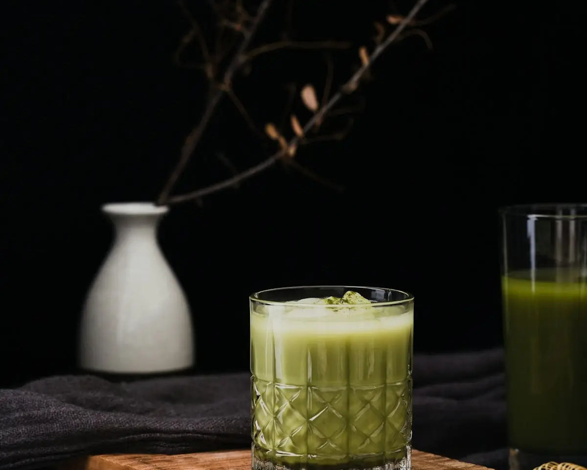 a glass of green juice next to a wooden cutting board