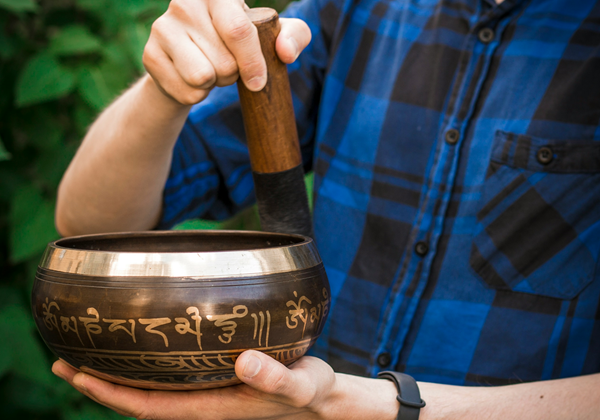 man rimming traditional metal tibetan singing bowl