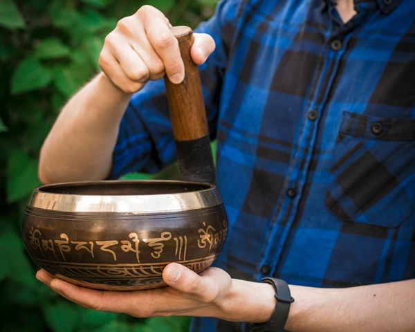 man rimming traditional metal tibetan singing bowl