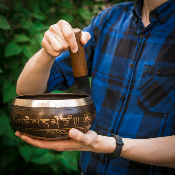 man rimming traditional metal tibetan singing bowl