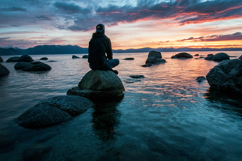 man meditating on rock at beach