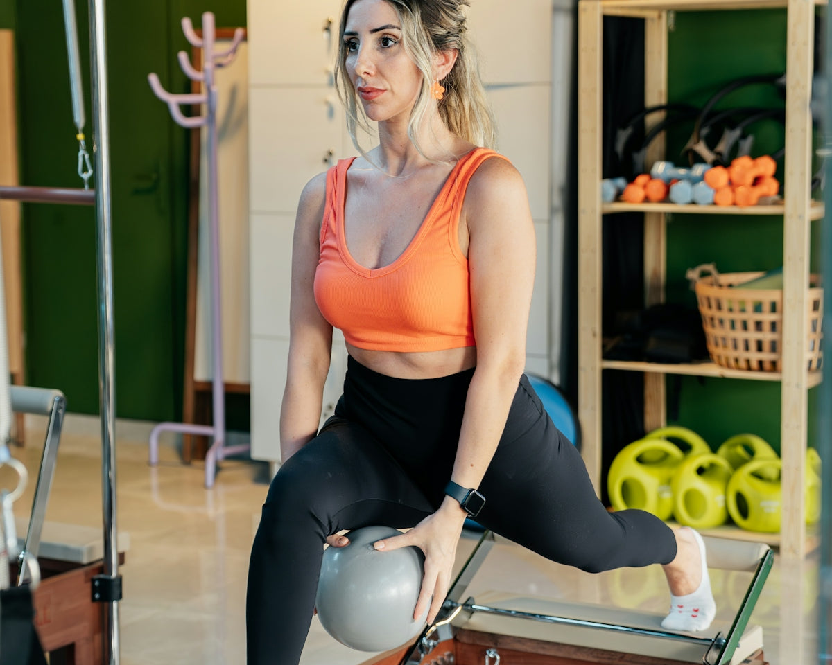 Woman practices lunges with a ball in a pilates studio.