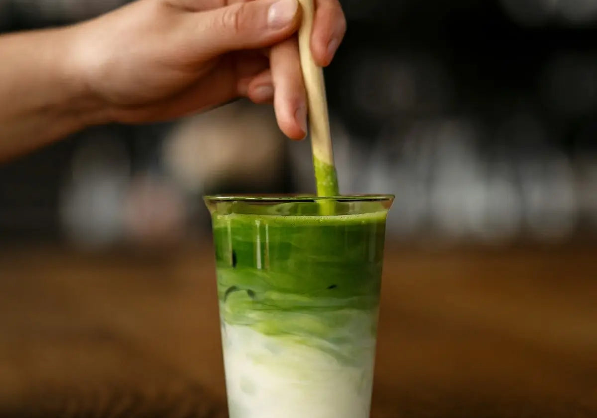 a hand holding a wooden stick over a green drink