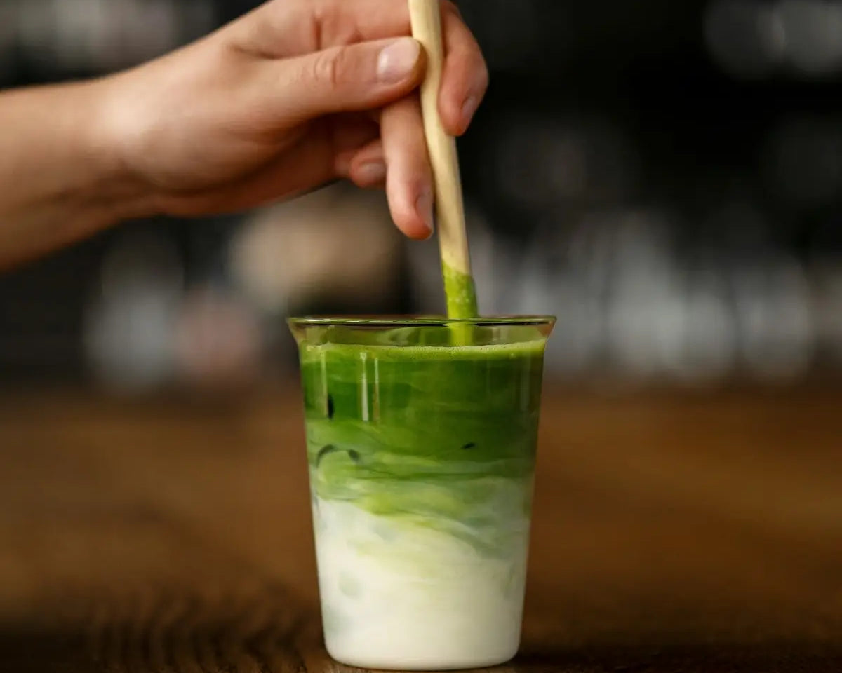 a hand holding a wooden stick over a green drink