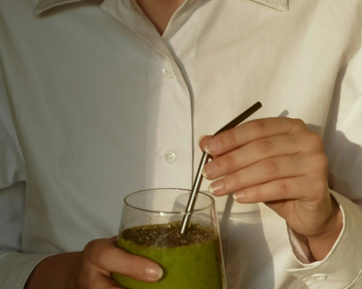 person in white button up shirt holding clear drinking glass with green liquid