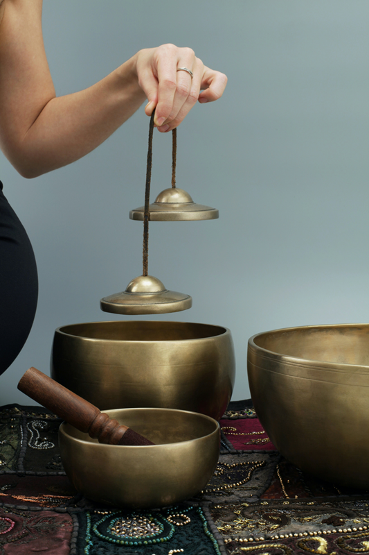 woman holding tibetan chime above a range of tibetan singing bowls