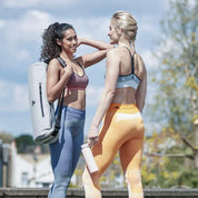 Two friends in athletic wear chatting outdoors with an Adidas Yoga Mat Carrier