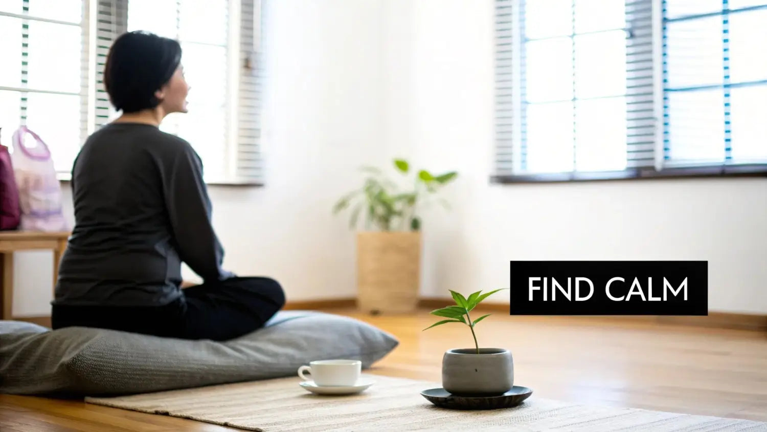 A woman meditates on a peaceful room, with a small plant and tea nearby.