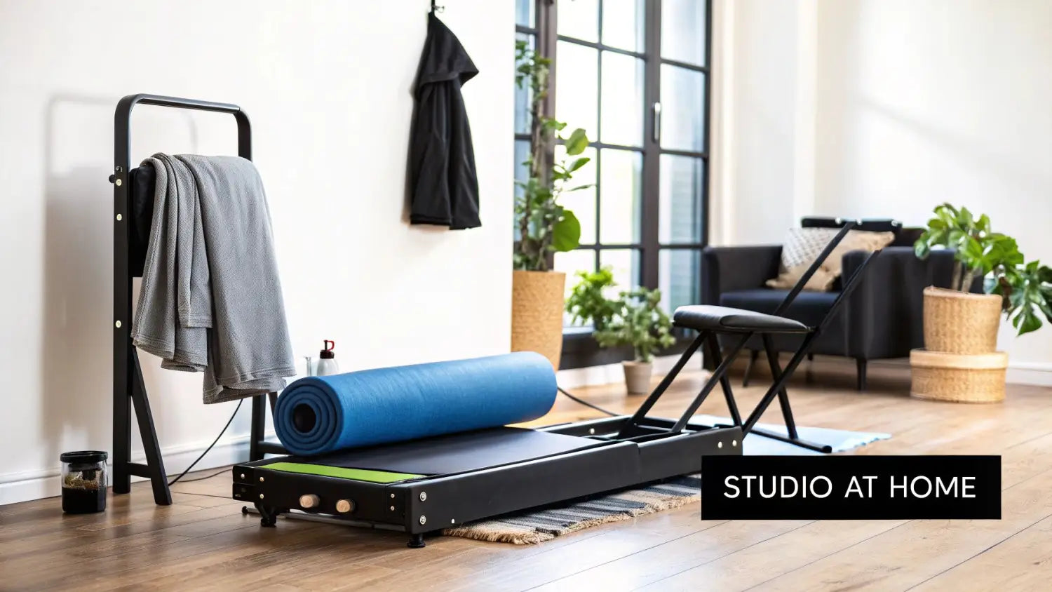 A foldable Pilates reformer machine with a blue mat and accessories in a bright home studio.