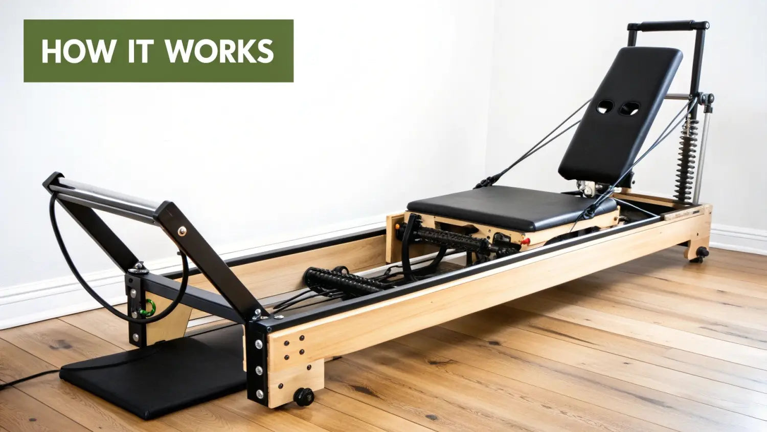 A light wood and black foldable Pilates reformer machine with an adjustable seat and straps.