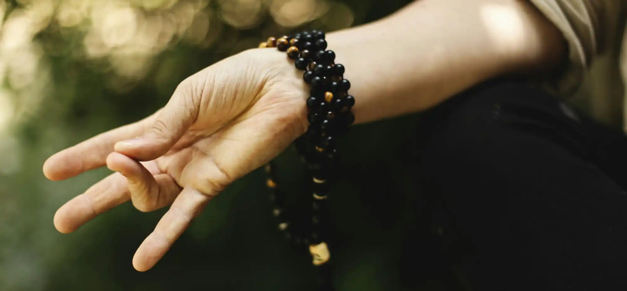 Hand wearing black beaded bracelets making a peace sign gesture.