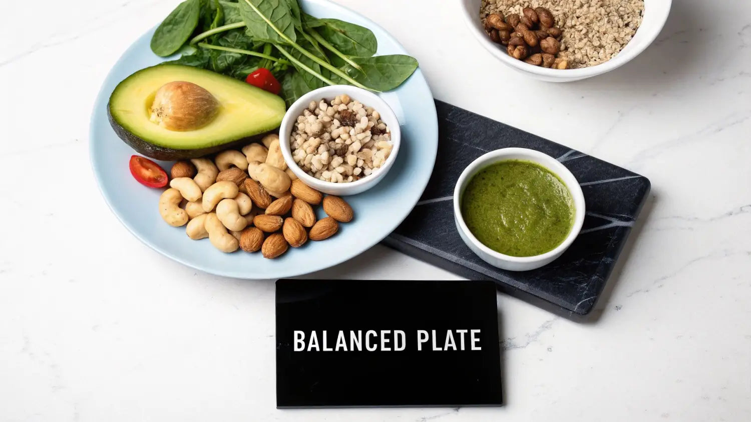 Overhead view of a balanced plate featuring avocado, spinach, nuts, grains, and green dressing.