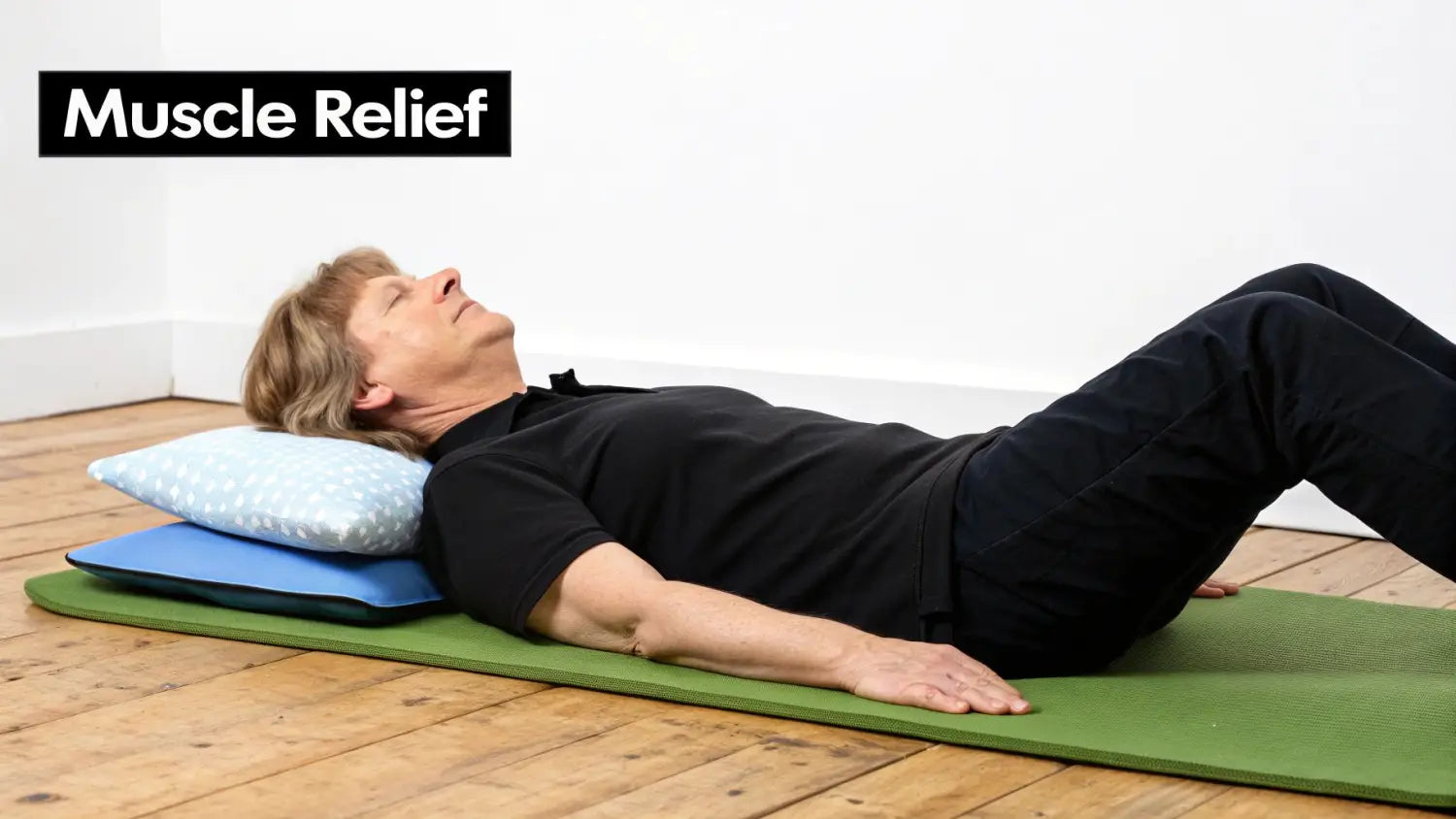 A person lies on their back on a green mat, knees bent, with two pillows supporting their head for muscle relief.