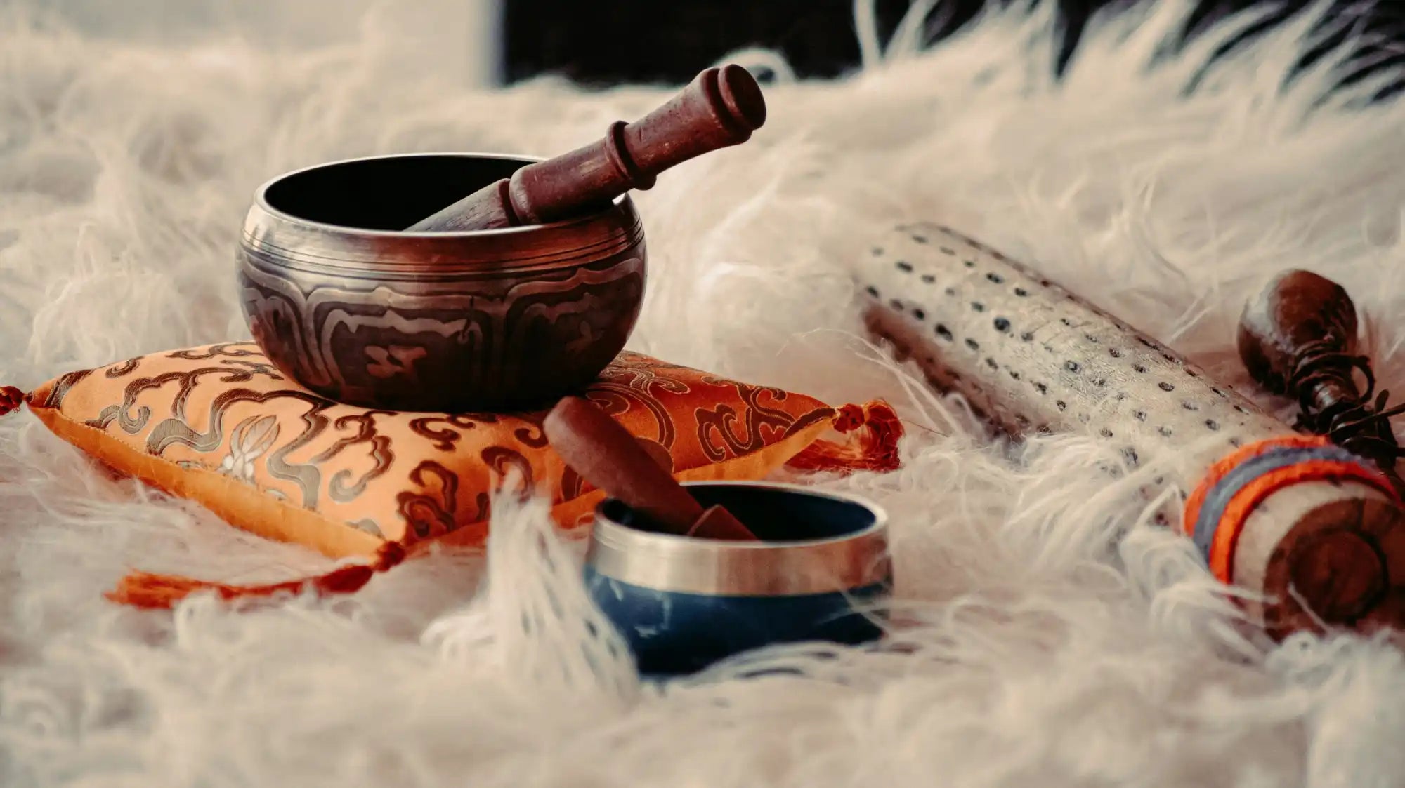 Tibetan singing bowl with wooden striker resting on orange fabric.