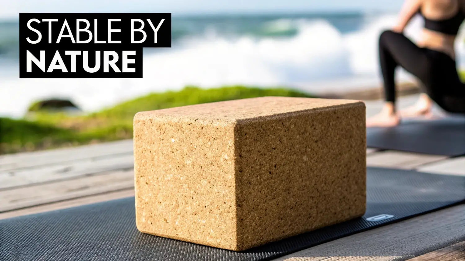 Cork yoga block placed on exercise mat outdoors near beach with person stretching in background